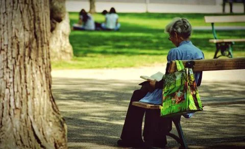 An old lady sitting on a bench in a park Stock Photos