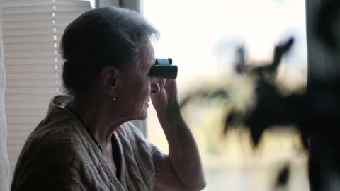 Old lady sitting by the window and looking through binoculars at home Stock Footage 189935981