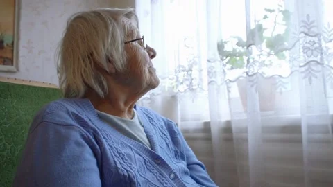Old lady smile at camera while sitting in a cozy chair next to the window	 Video stock 134022777