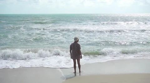 Old lady walking on beach with foaming waves. Slow motion Stock Footage 59854654
