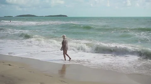 Old lady walking on beach with foaming waves. Slow motion Stock Footage 59854711