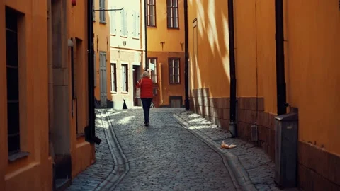 Old lady walks alone in a cobblestone alley. 库存影片 219197170