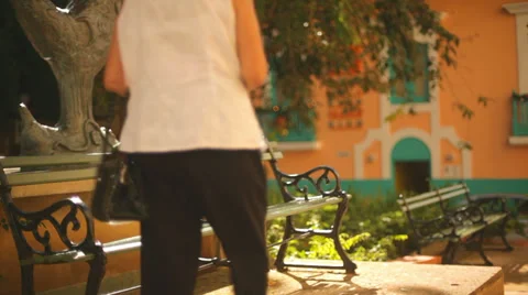 An old lady walks up to a bench, sits down and takes a tablet out of her bag 库存影片 33889411