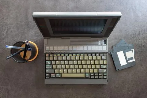 An old laptop computer next to some floppy disks Stock Photos