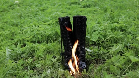 Old leather black high punk women's boots burn with fire standing on the grass Stock Footage 110776982