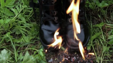 Old leather black high punk women's boots burn with fire standing on the grass Stock Footage 110777066
