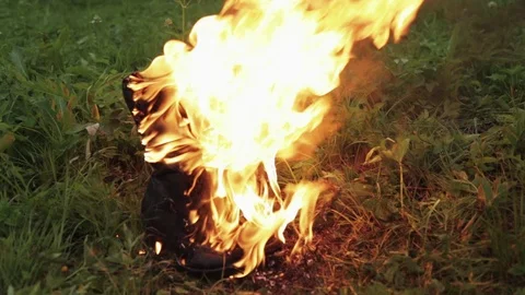 Old leather black high punk women's boots burn with fire standing on the grass Stock Footage 110777519
