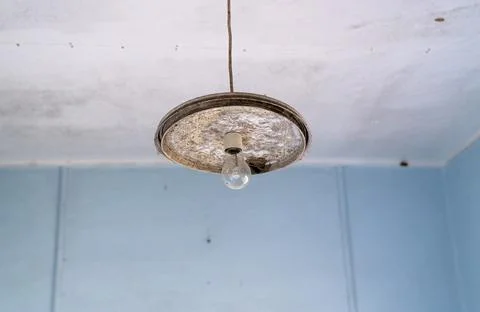 An old light bulb hangs from the ceiling in a worn-out room with peeling pain Stock Photos