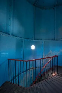 Old lighthouse on the inside. Red iron spiral stairs, round window and blue w Stock Photos