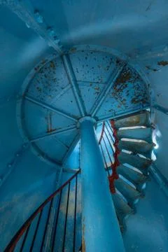 Old lighthouse on the inside. Red iron spiral stairs, round window and blue w Stock Photos