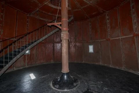 Old lighthouse on the inside. Red iron spiral stairs, round window and blue w Stock Photos