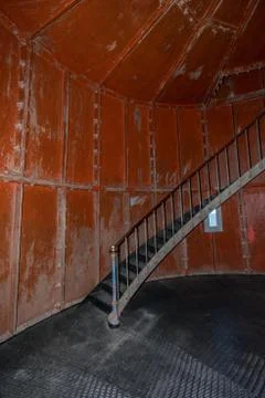 Old lighthouse on the inside. Red iron spiral stairs, round window and blue w Stock Photos