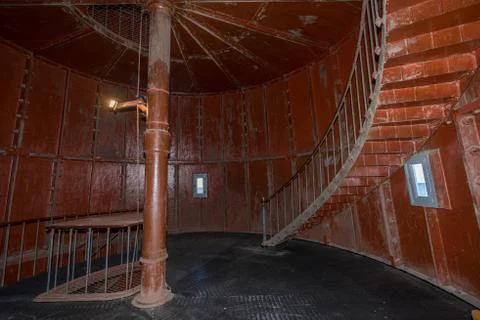 Old lighthouse on the inside. Red iron spiral stairs, round window and blue w Stock Photos