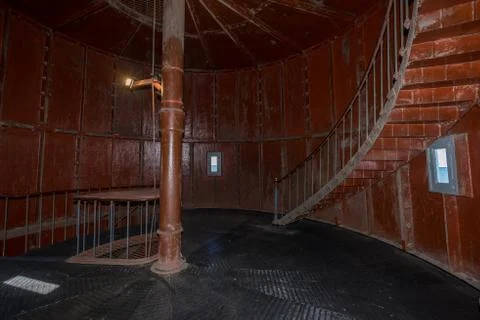 Old lighthouse on the inside. Red iron spiral stairs, round window and blue w Stock Photos