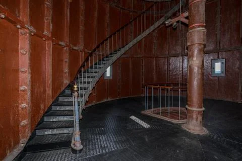 Old lighthouse on the inside. Red iron spiral stairs, round window and blue w Stock Photos