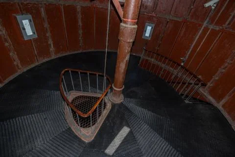 Old lighthouse on the inside. Red iron spiral stairs, round window and blue w Stock Photos