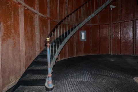 Old lighthouse on the inside. Red iron spiral stairs, round window and blue w Stock Photos