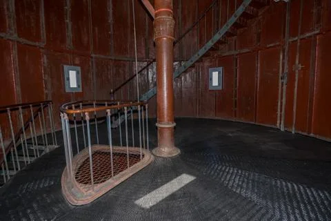 Old lighthouse on the inside. Red iron spiral stairs, round window and blue w Stock Photos