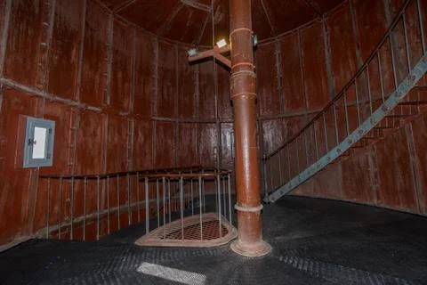 Old lighthouse on the inside. Red iron spiral stairs, round window and blue w Stock Photos