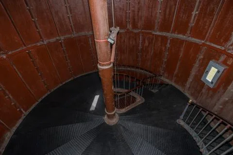 Old lighthouse on the inside. Red iron spiral stairs, round window and blue w Stock Photos