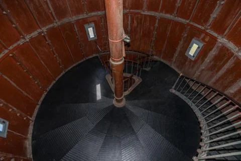 Old lighthouse on the inside. Red iron spiral stairs, round window and blue w Stock Photos