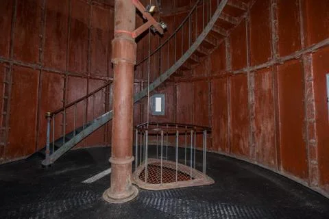 Old lighthouse on the inside. Red iron spiral stairs, round window and blue w Stock Photos
