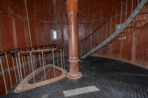 Old lighthouse on the inside. Red iron spiral stairs, round window and blue w Stock Photos