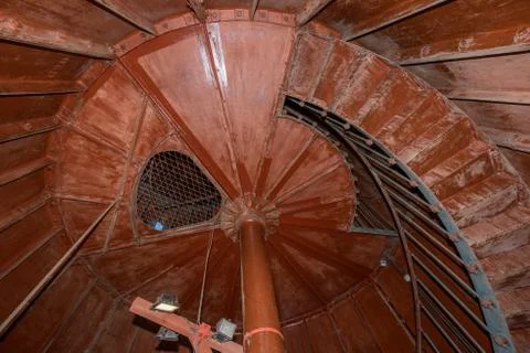 Old lighthouse on the inside. Red iron spiral stairs, round window and blue w Stock Photos