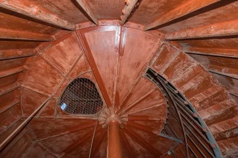 Old lighthouse on the inside. Red iron spiral stairs, round window and blue w Stock Photos