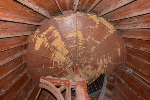 Old lighthouse on the inside. Red iron spiral stairs, round window and blue w Stock Photos