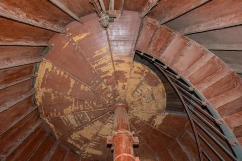 Old lighthouse on the inside. Red iron spiral stairs, round window and blue w Stock Photos