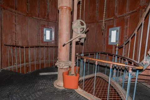 Old lighthouse on the inside. Red iron spiral stairs, round window and blue w Stock Photos