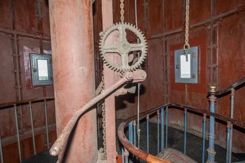 Old lighthouse on the inside. Red iron spiral stairs, round window and blue w Stock Photos