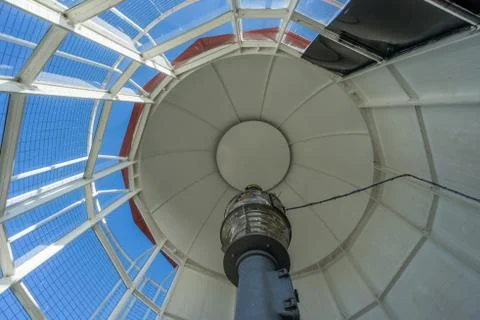 Old lighthouse on the inside. Red iron spiral stairs, round window and blue w Stock Photos