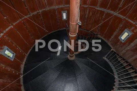 Old lighthouse on the inside. Red iron spiral stairs, round window and ...