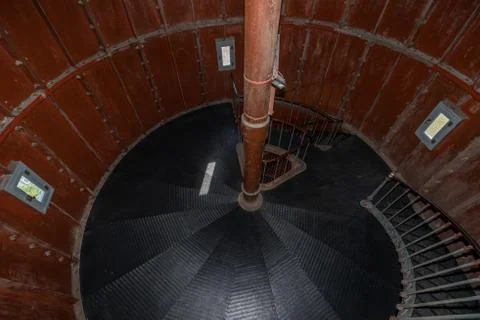 Old lighthouse on the inside. Red iron spiral stairs, round window and blue w Stock Photos
