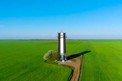Old lighthouse with red stripes in spring field. Scenic landscape  Stock Photos