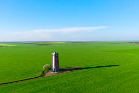 Old lighthouse with red stripes in spring field. Scenic landscape  Stock Photos