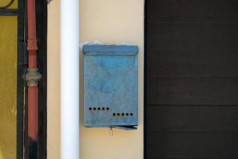 An old mailbox hangs on the wall between the pipe and the gate. Nobody Stock Photos
