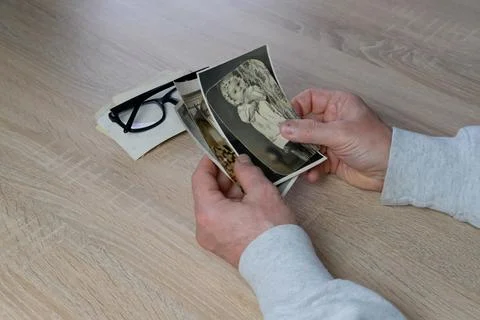 Old male hands hold retro family photos over an album with vintage monochrome Stock Photos