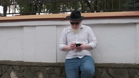Old man with albinism browsing on the internet while sitting next to his house. Stock Footage 147138912