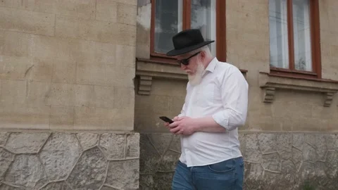 Old man with albinism browsing on the internet while walking next to old house. Stock Footage 148945802