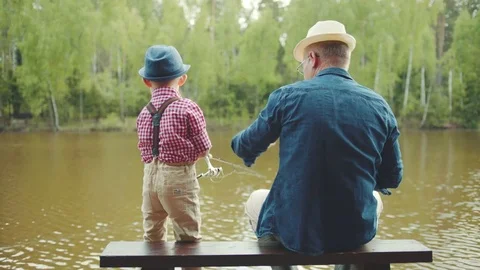 Old man and his grandson in straw hats are fishing on the river at summertime Stock Footage