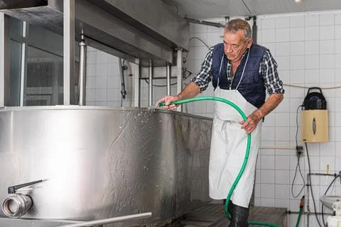 Old man in an apron rinse down soap from a stainless steel container Stock Photos