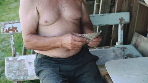 Old man with bare torso playing cards and sitting on old blue bench outside Stockbeeldmateriaal 134421212