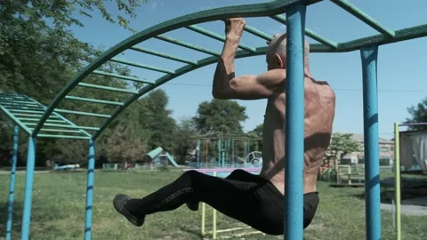 Old man with bare torso shows trick on crossbar on sunny day Stock Footage 201552088