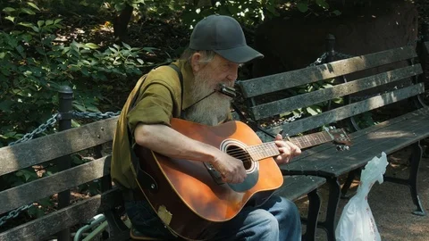 Old Man on Bench Playing Guitar and Harmonica in Park Stock Footage 104890935