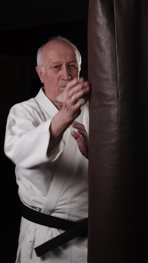 Old man with black belt performs powerful circular punches on the machine Stock Footage 309750901