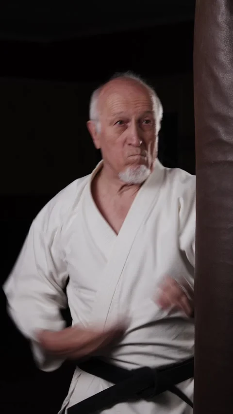 Old man with black belt practicing circular punches on the machine Video stock 309750942