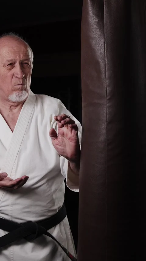 Old man with black belt practicing powerful circular punches on the machine Stock Footage 309750944